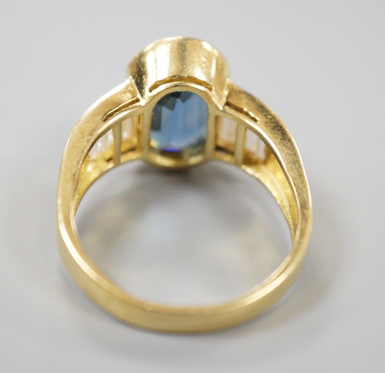 A modern 18ct gold and single stone oval cut sapphire set ring, with baguette cut diamond set shoulders, size R, gross weight 8.3 grams.